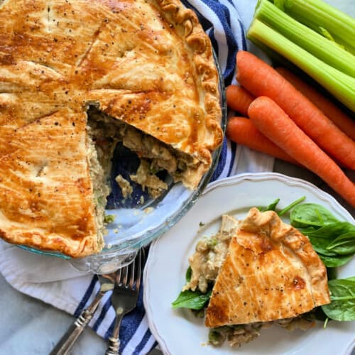 Pie with a slice taken out and a piece of savory pie resting on spinach on a white plate.