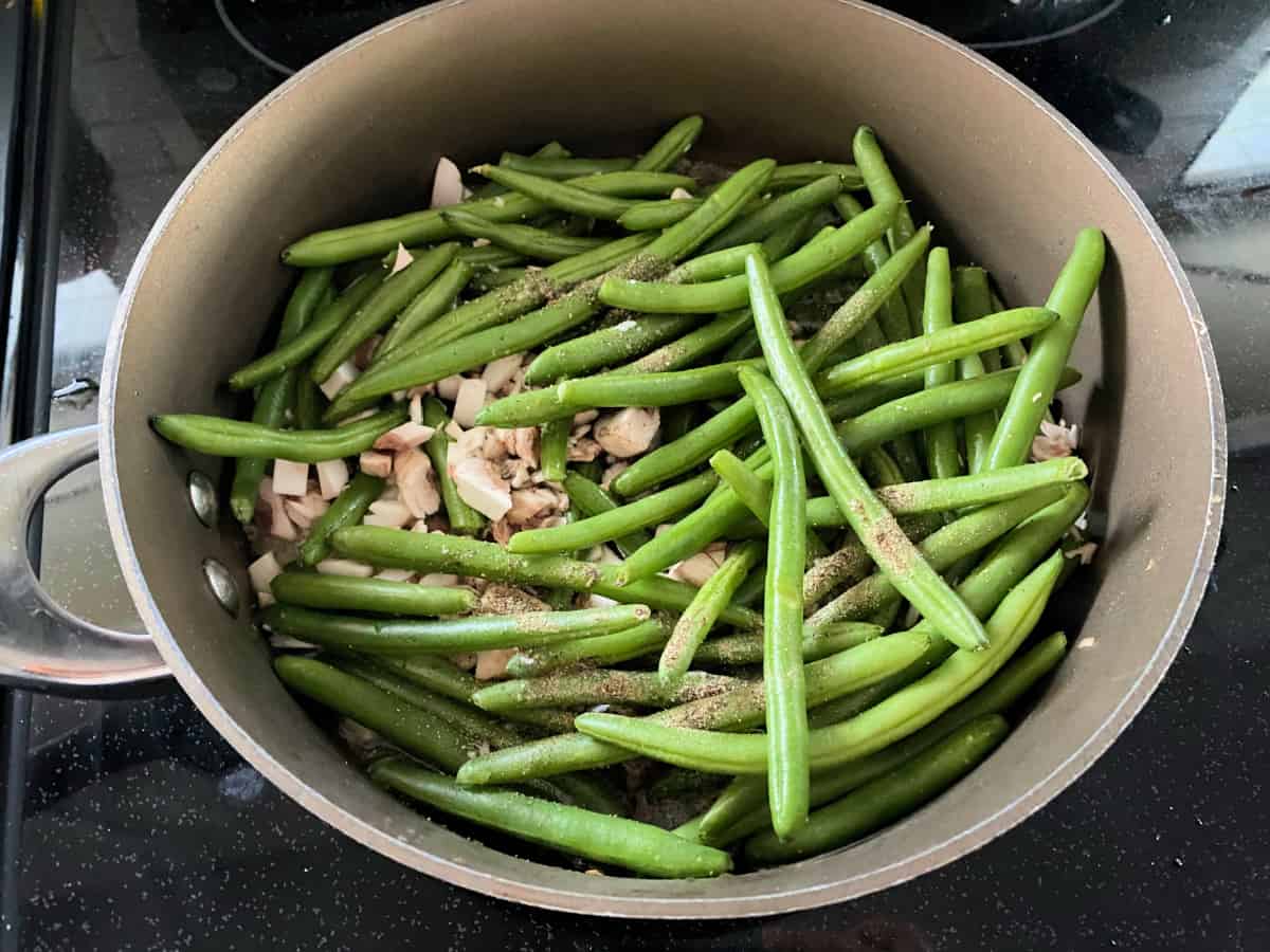 Raw green beans, mushrooms, and seasoning in a skillet.