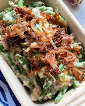 Close up of baking dish with green bean casserole on a blue and white striped cloth.