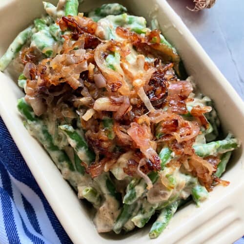 Close up of baking dish with green bean casserole on a blue and white striped cloth.