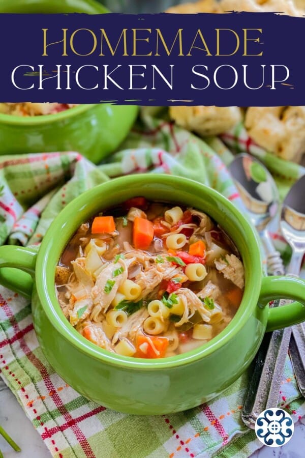 Text on image: "homemade chicken soup" with close up image of green bowl with italian chicken soup on a green and pink plaid cloth, with two spoons and bread in the background.