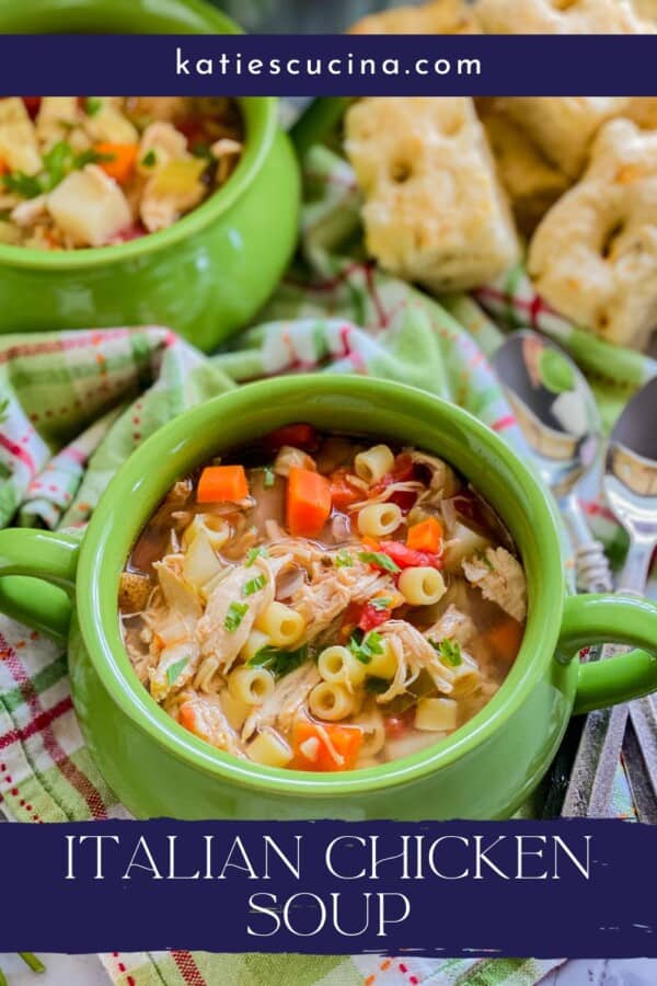 Text on image: "italian chicken soup" with photo of two green bowls with italian chicken soup on a green and pink plaid cloth, two overlapping spoons, and bread in the background.