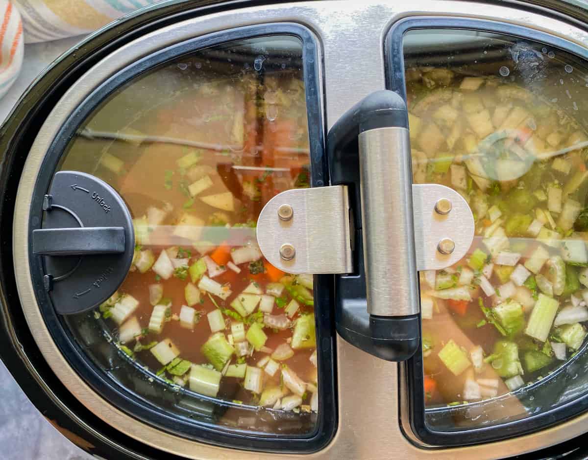 Slow cooker with filled with ingredients and chicken broth with lid on top.