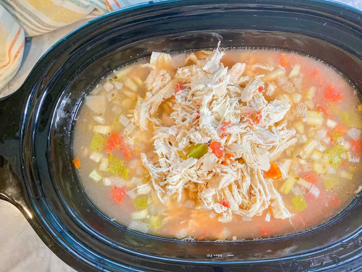 Slow cooker with filled with ingredients and chicken broth with shredded chicken on top