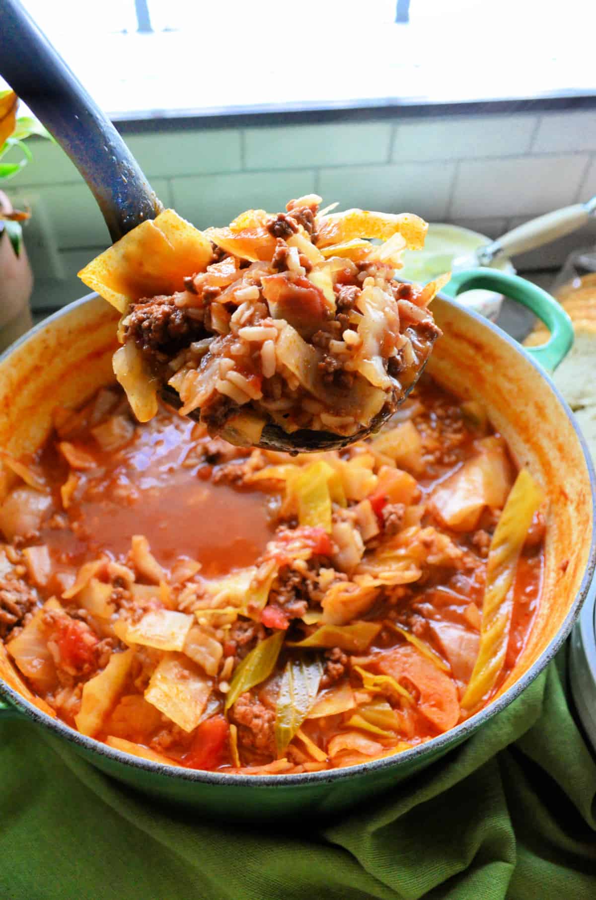 a pot full of cabbage soup on green fabric and a ladle with soup.