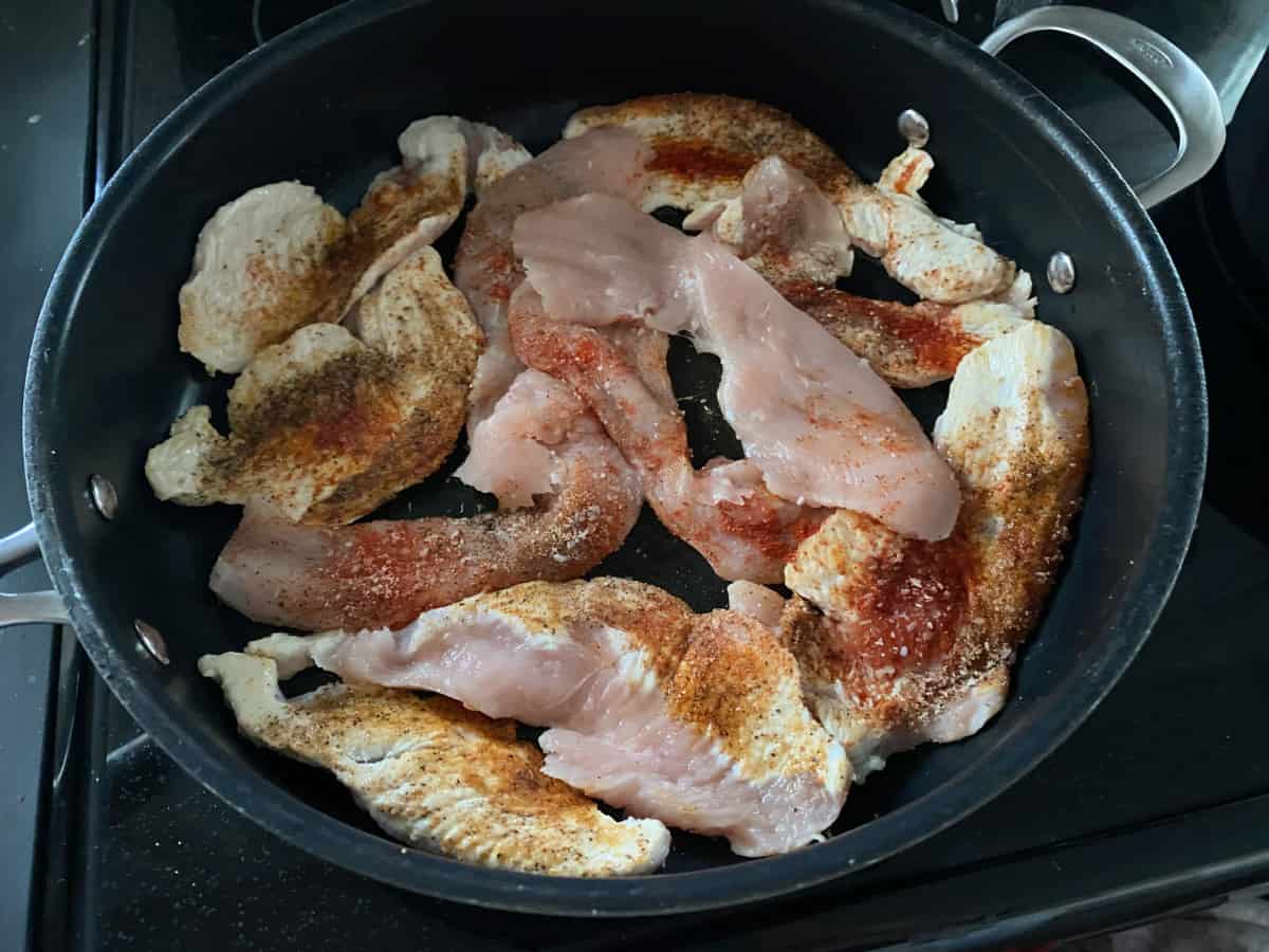 Seasoned turkey breast cutlets cooking in a pan.
