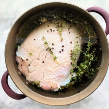 Brown pot on a marble countertop with a raw turkey breast and spices inside it.