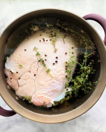 Brown pot with a turkey peppercorns, and fresh thyme in water on a marble countertop.