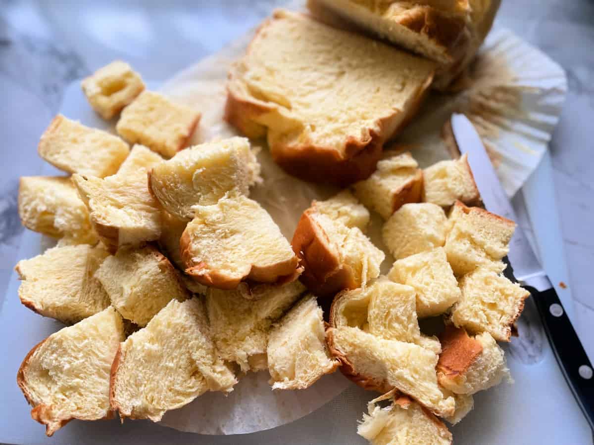 Cubes of brioche bread cut with slices of brioche and a serrated knife in the background.