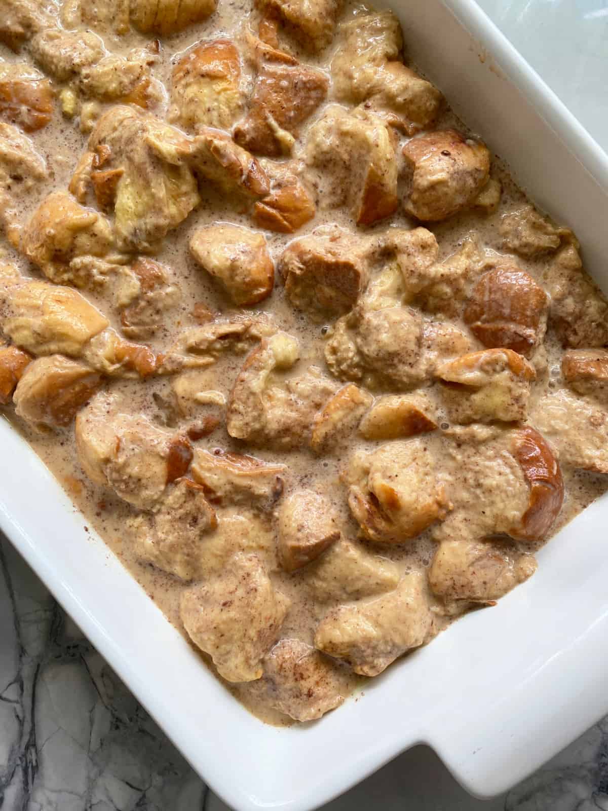 White baking dish filled with custard and chopped up bread.