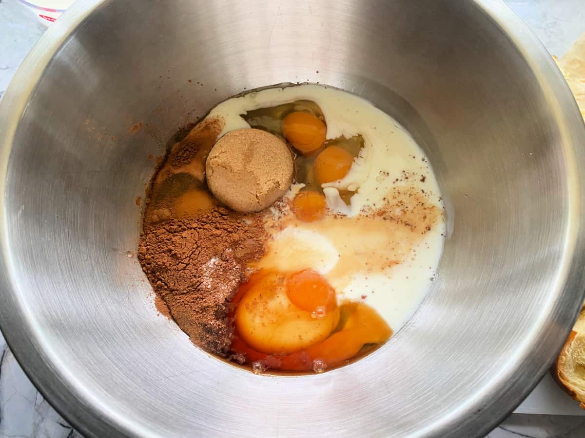 Silver bowl filled with milk, eggs, brown sugar, cinnamon, and vanilla extract.