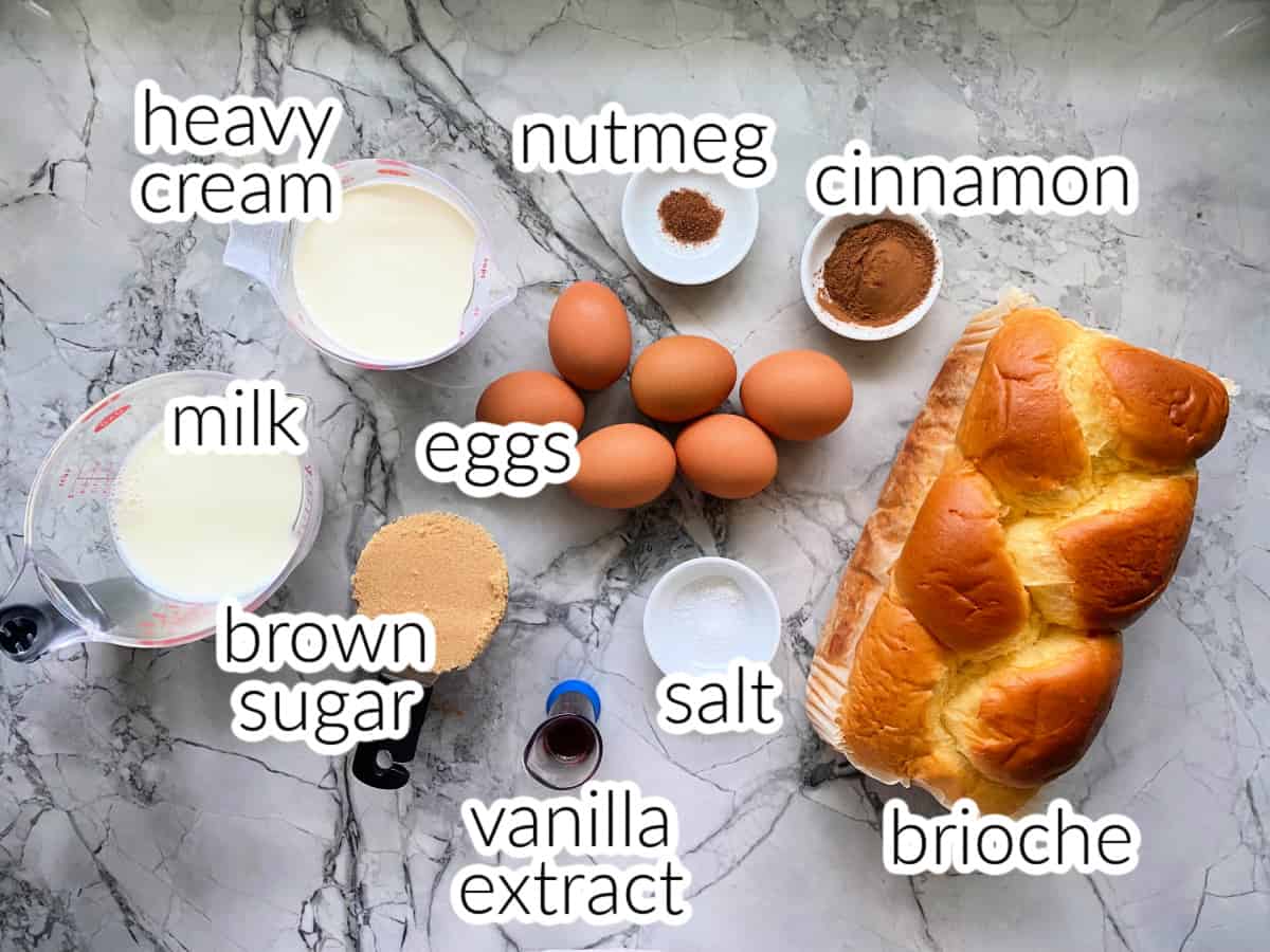 Ingredients on counter: brioche, eggs, cinnamon, nutmeg, heavy cream, milk, brown sugar, vanilla extract, and salt.