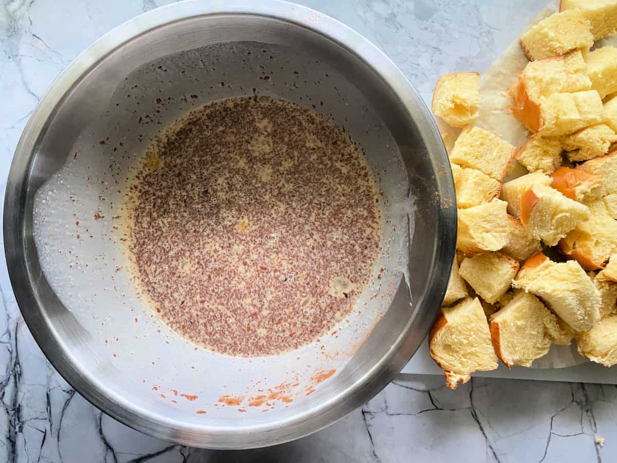 White bowl filled with cinnamon custard mixture with bread next to it.