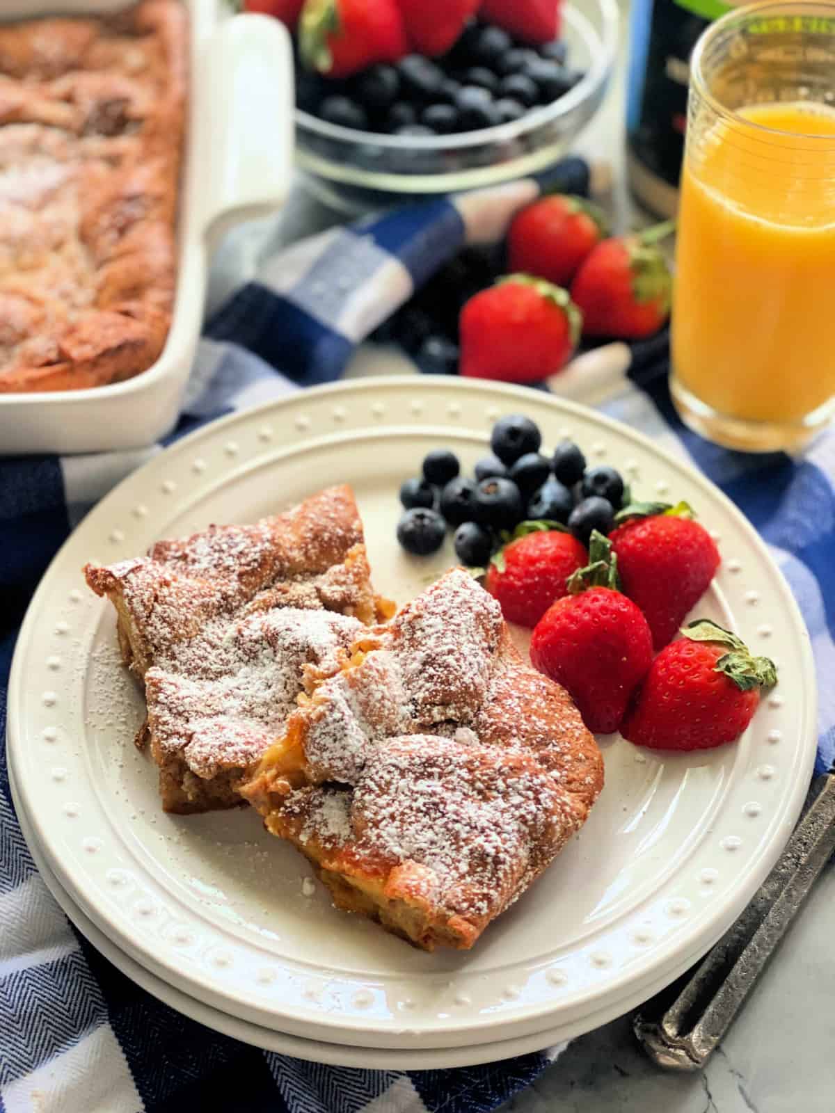 Two stacked white plates with two slices of french toast bake and berries.