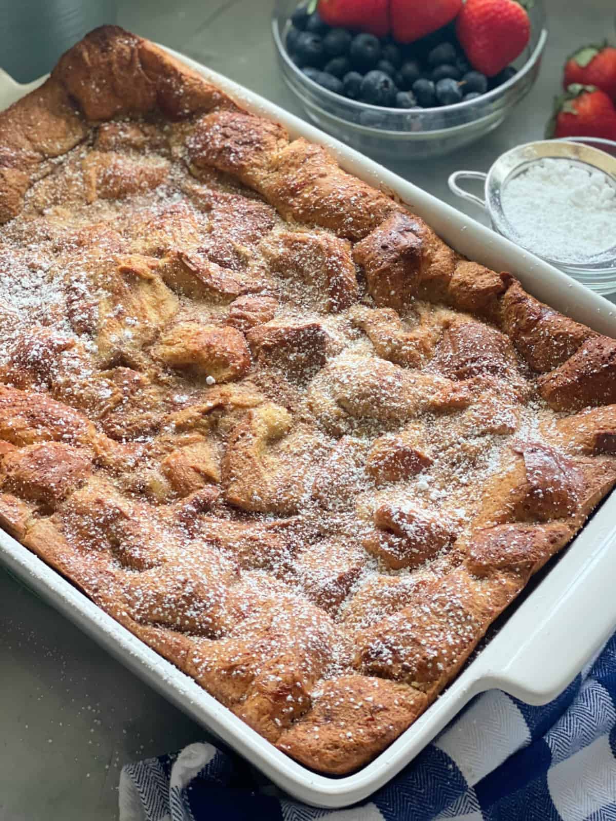 White baking dish with baked french toast with powder sugar on top.