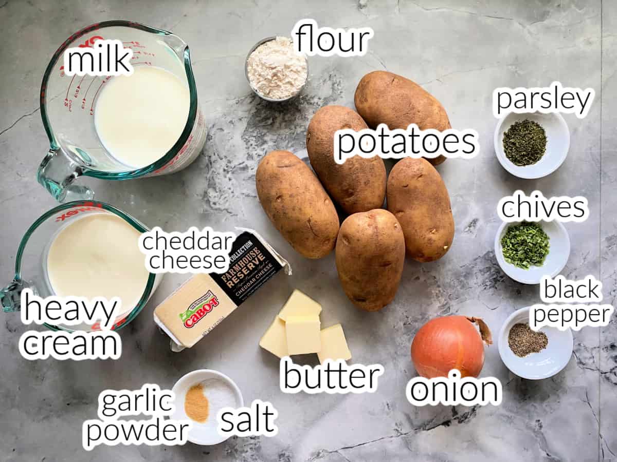 Ingredients for cheesy scalloped potatoes with milk, flour, cheddar cheese, heavy cream, garlic powder, salt, butter, potatoes, onion, black pepper, chives, and parsely.