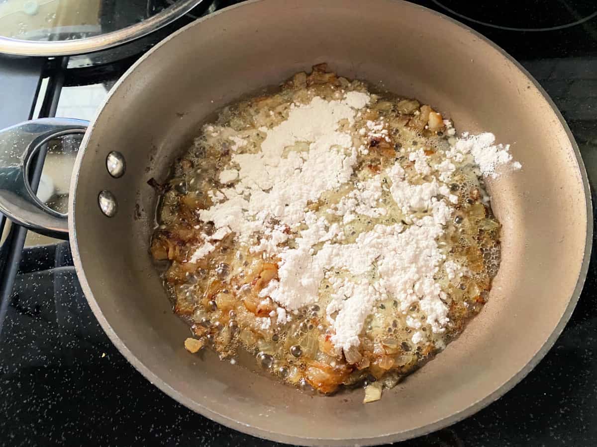 Ingredients for onions with flour being added to the saucepan on top of the stove top.