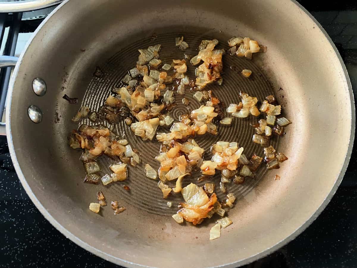 Onions being sautéed in a saucepan on top of the stove top.