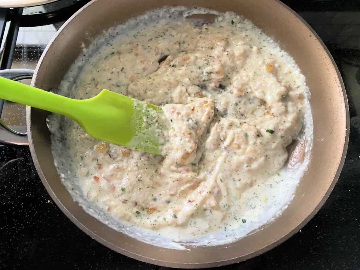 Cream sauce getting mixed with a green spatula in a saucepan on the stovetop.