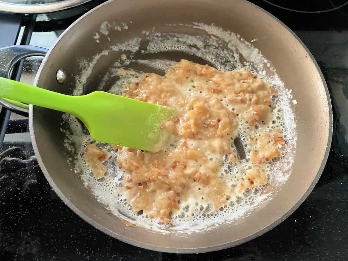 Onion being cooked in the saucepan on the stovetop with a green spatula.