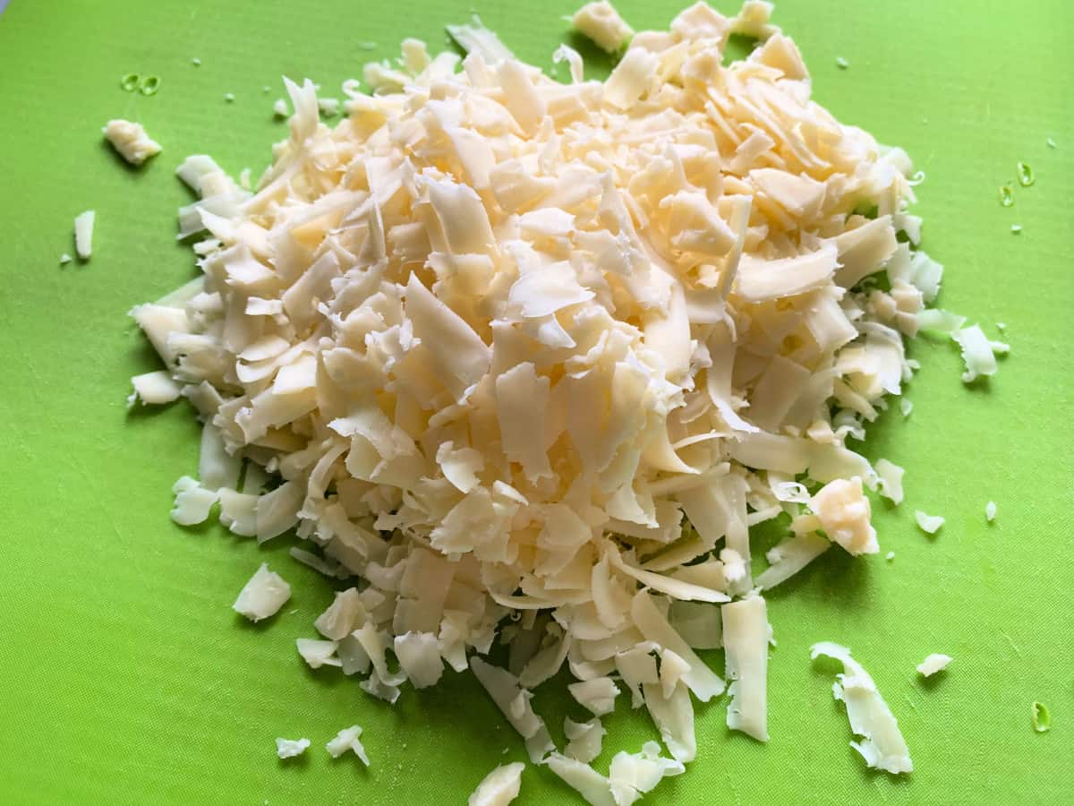 Green cutting board with white shredded cheddar cheese.