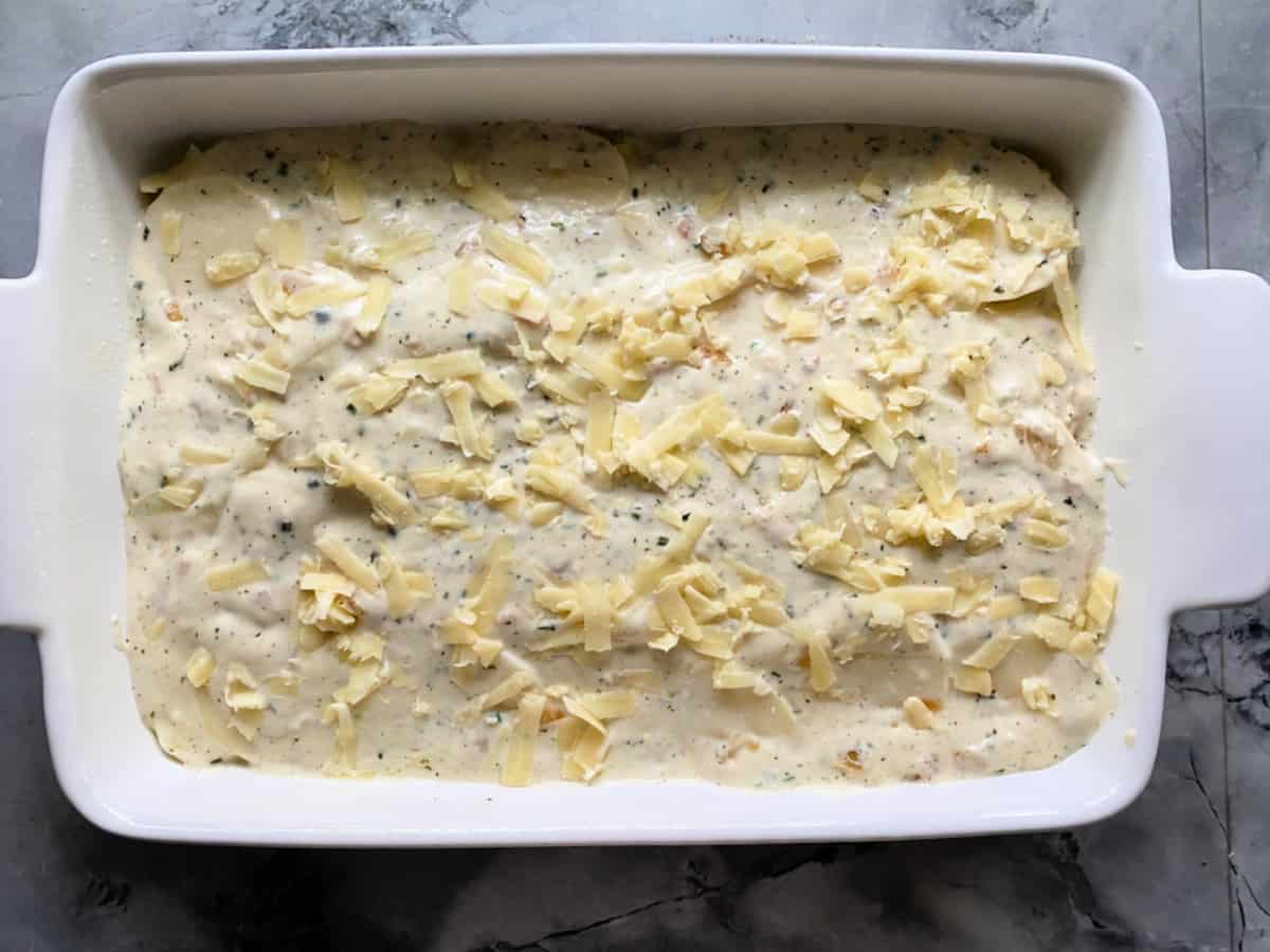 Marble countertop with a white casserole dish filled with a cream sauce and shredded cheese.