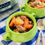 Two green bowls filled with beef stew with a white and blue checkered cloth underneath the bowls.