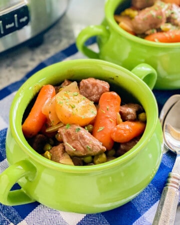 Two green bowls filled with beef stew with a white and blue checkered cloth underneath the bowls.