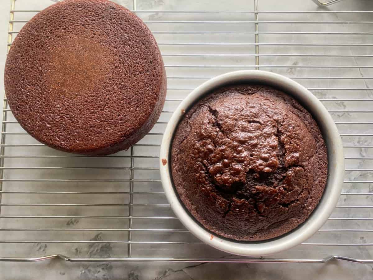 Cooked chocolate cake with one outside the cake pan and the other inside the cake pan on top of a cooling rack.