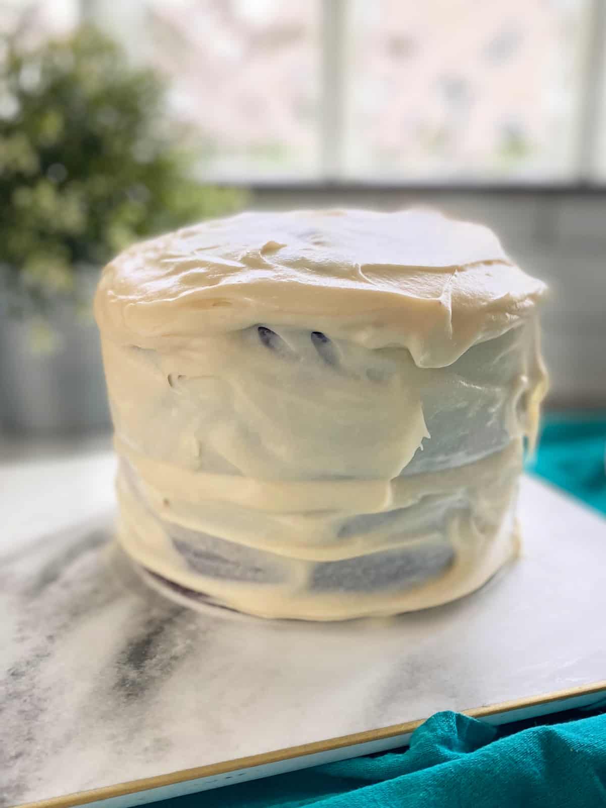 Chocolate cake covered with cream cheese frosting on marble counter top.