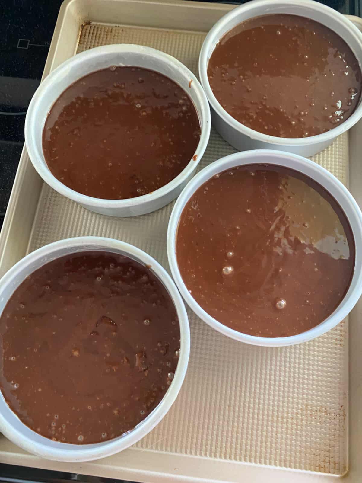 Chocolate cake batter in four cake pans.