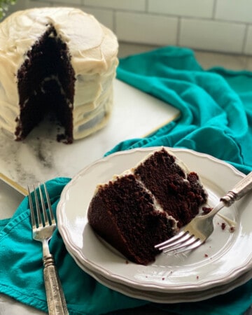 A slice of chocolate cake on a white plate with a two layer cake in the background.