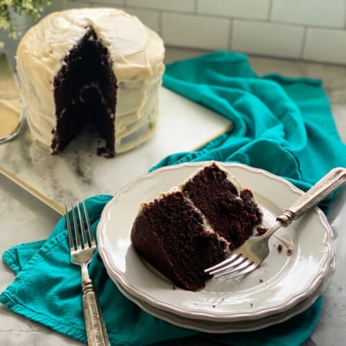 A slice of chocolate cake on a white plate with a two layer cake in the background.