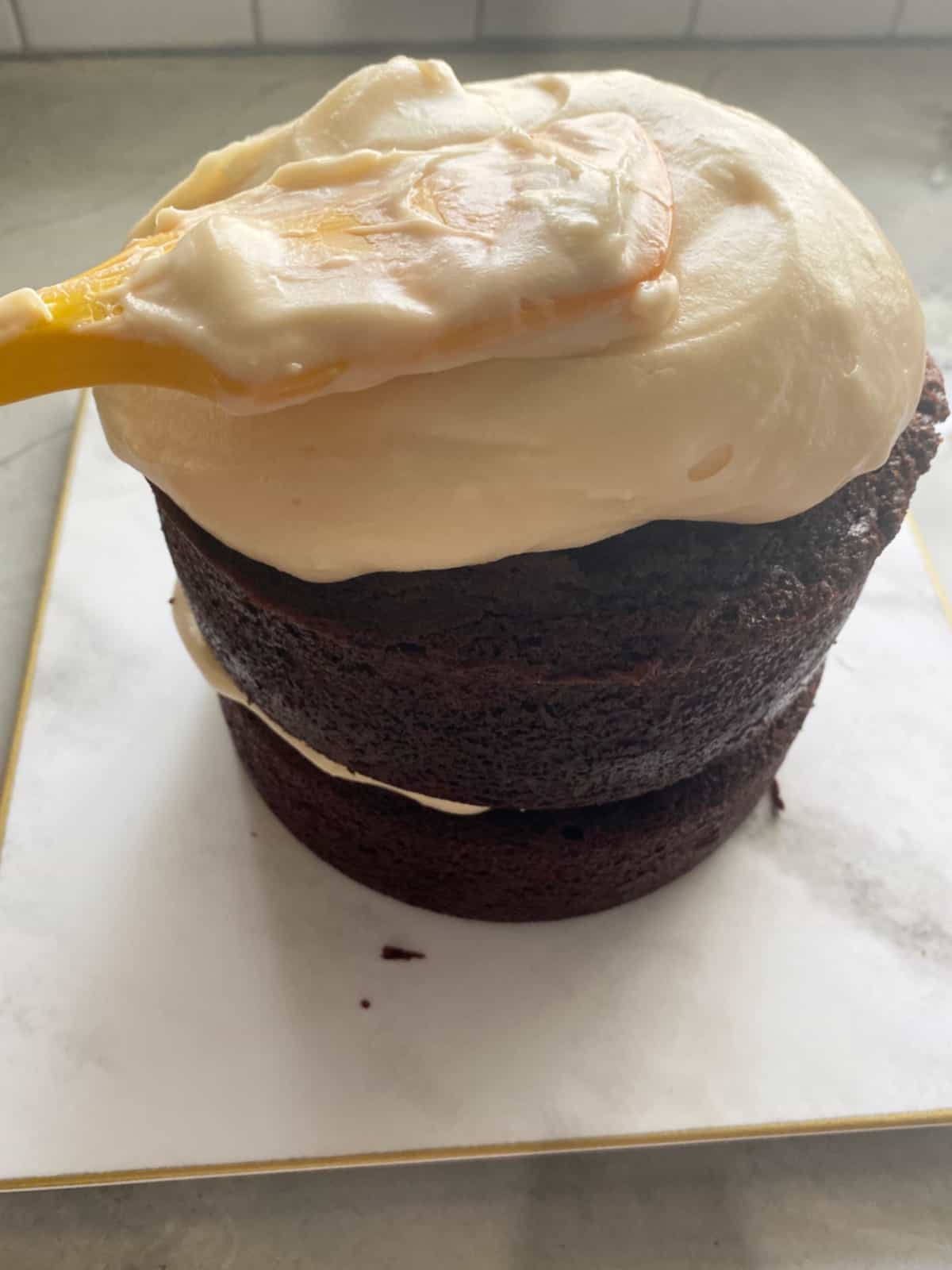 Chocolate cake being frosted with cream cheese frosting.