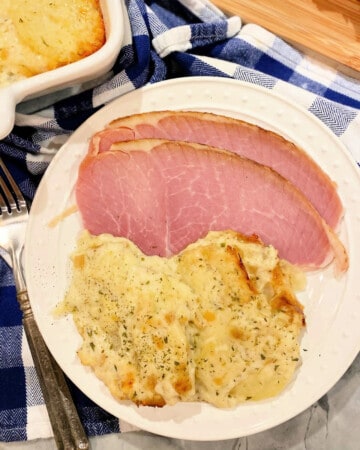 White plate filled with sliced ham and scalloped potatoes.