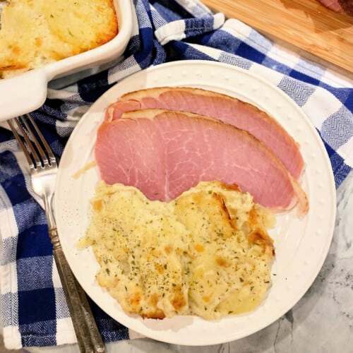 White plate filled with sliced ham and scalloped potatoes.