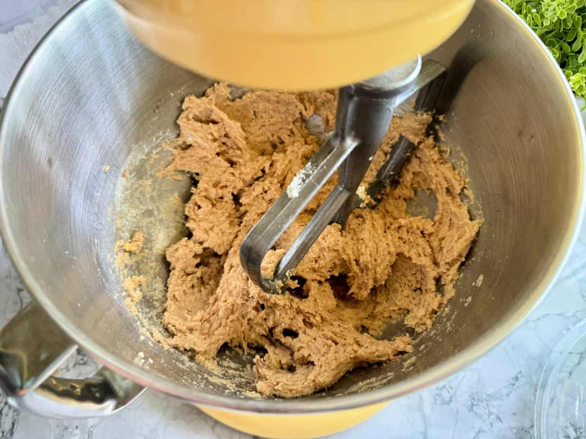 Yellow stand mixer with flat paddle and dough in bowl.