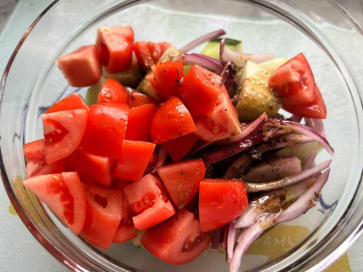 Glass bowl with chopped tomatoes, onions, and cucumbers with dressing.