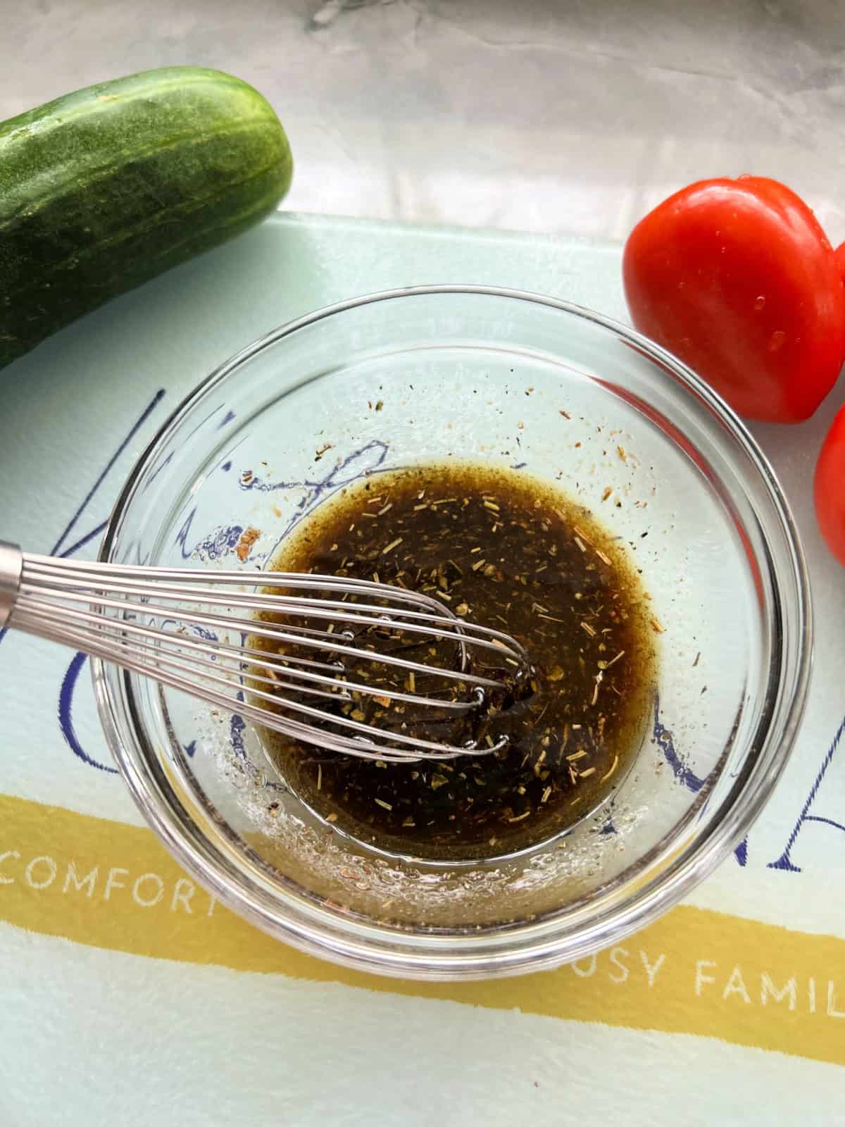 Glass bowl with dressing and a whisk on a cutting board.