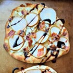 Square picture of a flatbread with bacon, sliced pears, and balsamic dressing.