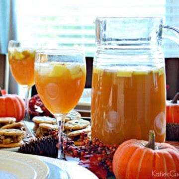 Glass pitcher and two wine glasses filled with a brown sangria and diced apples.