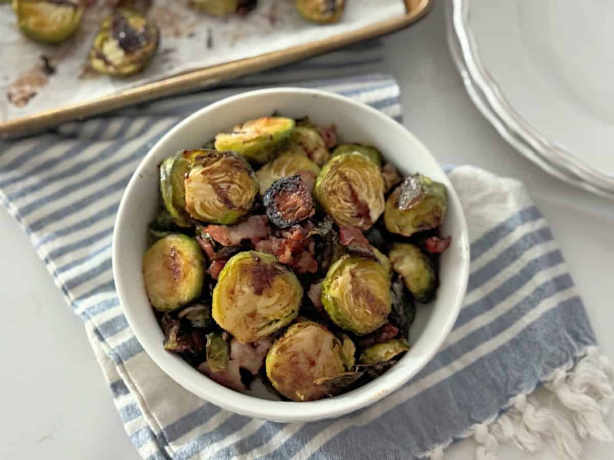White bowl on a blue and white cloth filled with brussels sprouts.