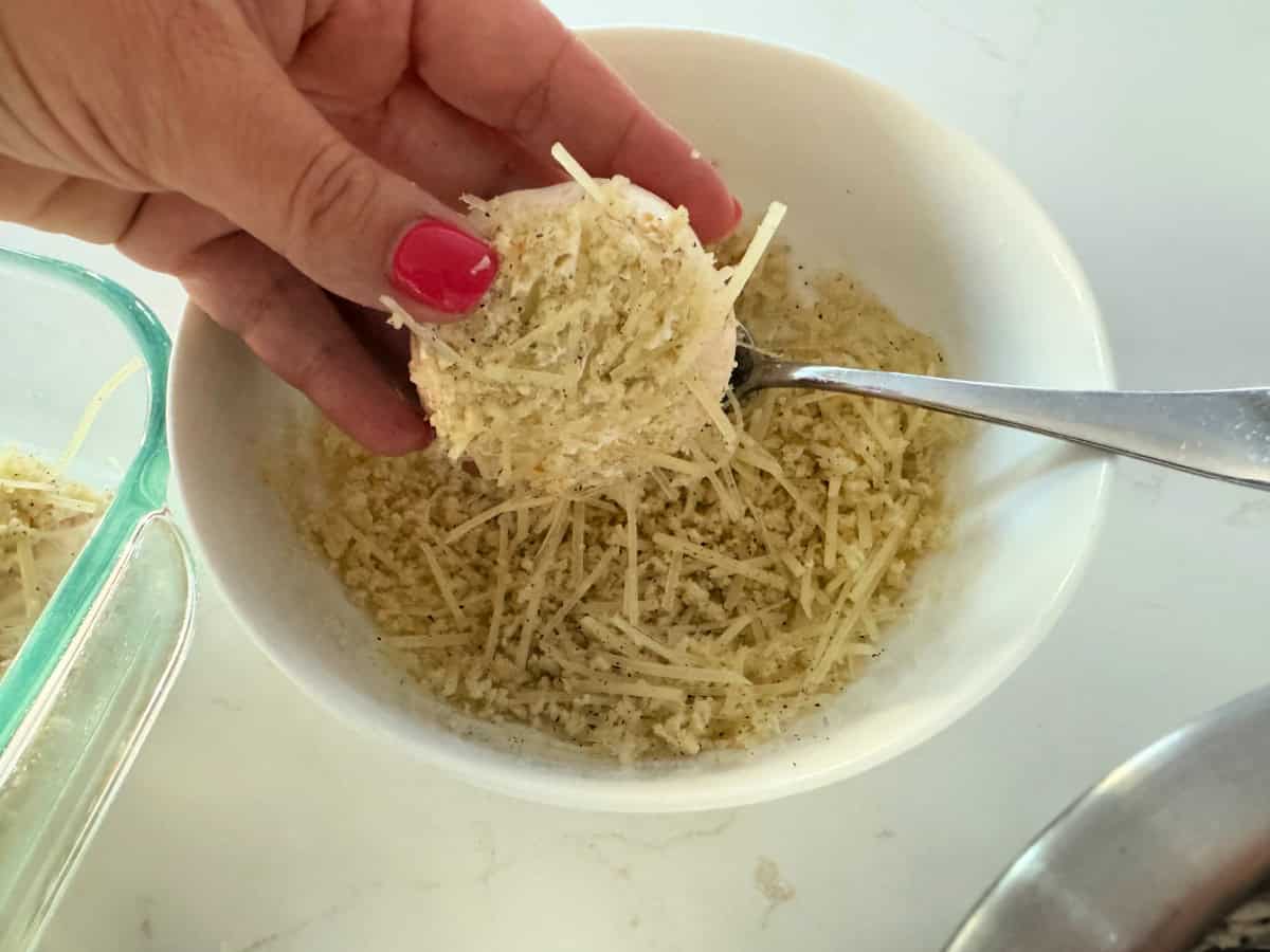 Female hand with pink nails holding a raw stuffed mushroom with breaded topping over a bowl.