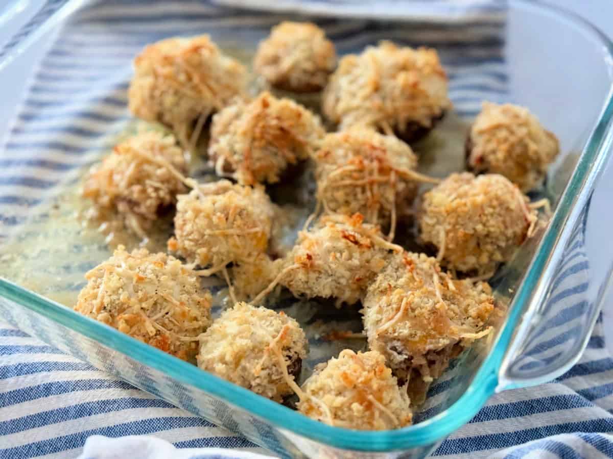 Square glass baking dish on top of a white and blue striped cloth with cooked stuffed mushrooms.