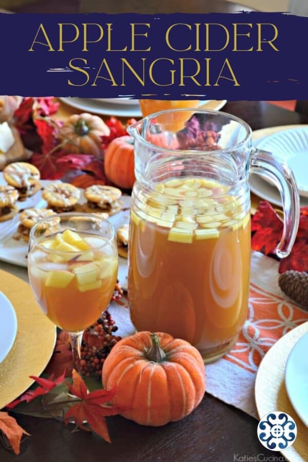 Pitcher of apple sangria with a wine glass filled with sangria on a beautiful fall table with text on image for Pinterest.