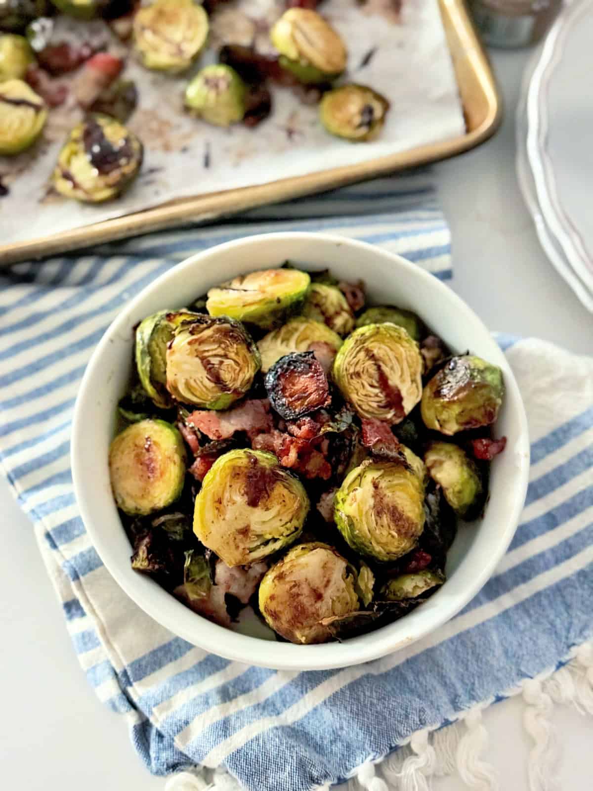 White bowl filled with sliced roasted brussels sprouts with bacon on a white countertop.
