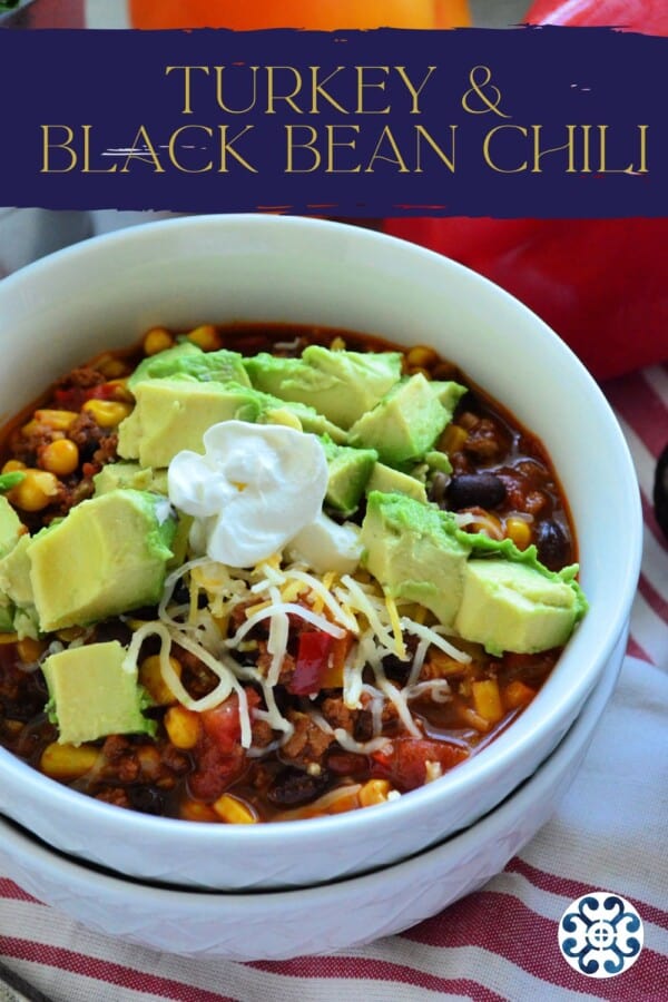 Two white bowls stacked with chili and topped with shredded cheese, sour cream, and avocado slices with text on image for Pinterest.