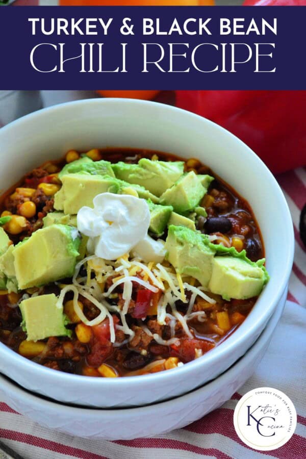 Two white bowls stacked with top bowl filled with chili, cheese, avocados, and sour with text on image for Pinterest.