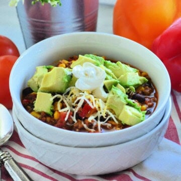 Two white bowls filled with chili and topped with shredded cheese, diced avocado and a dollop of sour cream.