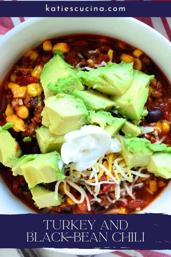 Chili, corn, black beans, avocado, cheese and sour cream in a white bowl with text on image for Pinterest.